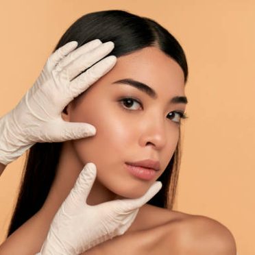 Young Asian woman with clean radiant skin gets botox injections for contour tightening, lip augmentation on a beige background. Spa care, facial skin care, beauty cosmetology.